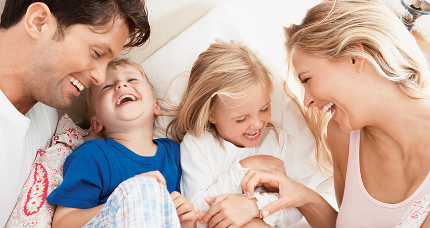 A young family with two young kids laughing as their parents tickle them